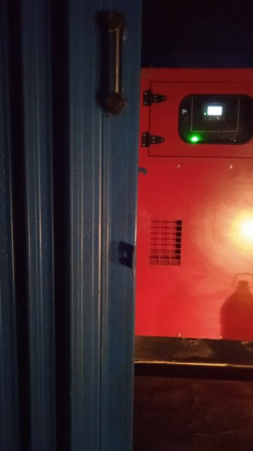 Genset merah di balik pintu gulung berwarna biru